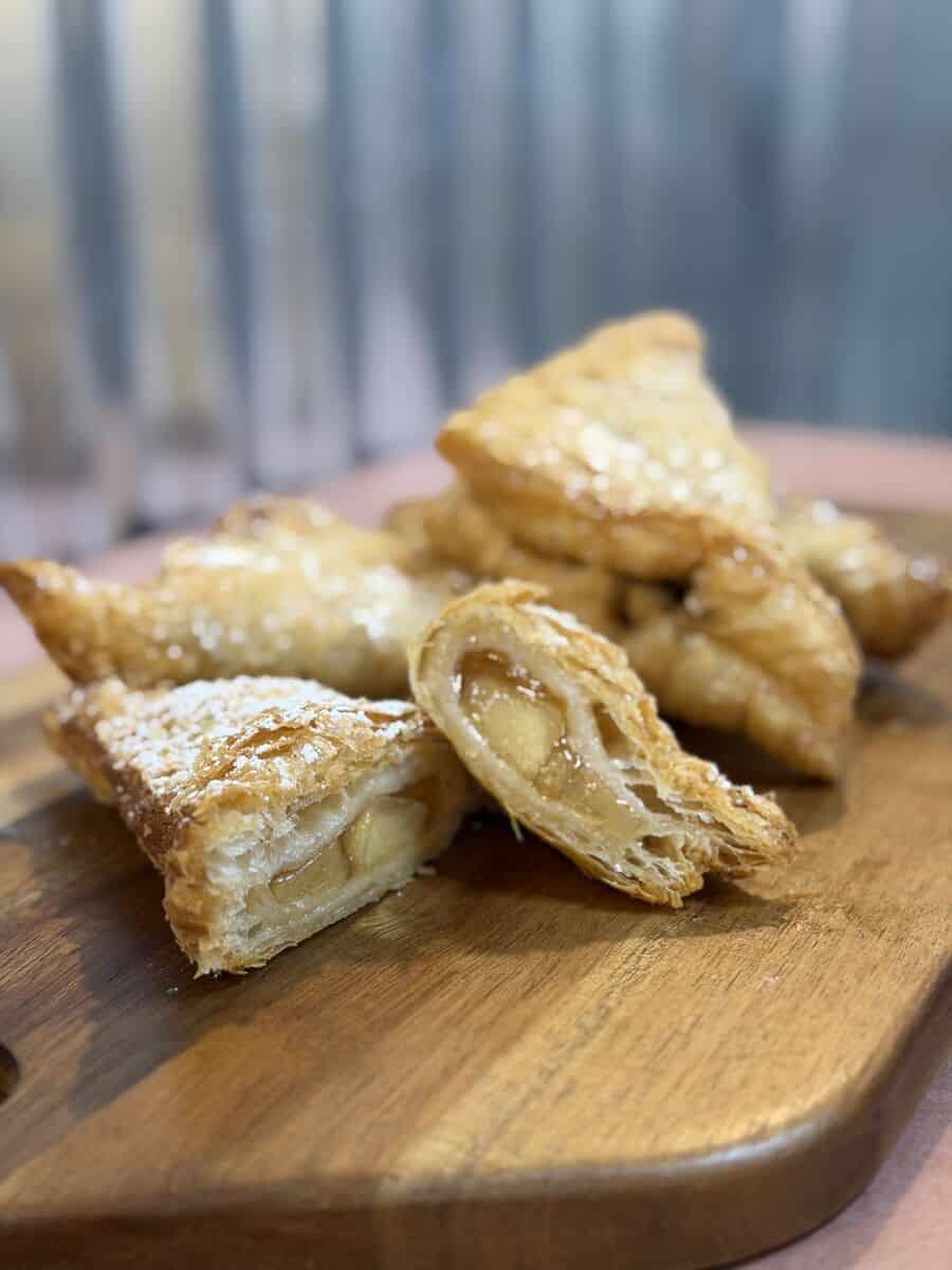 Golden fried fruit turnovers dusted with powdered sugar on a wooden cutting board