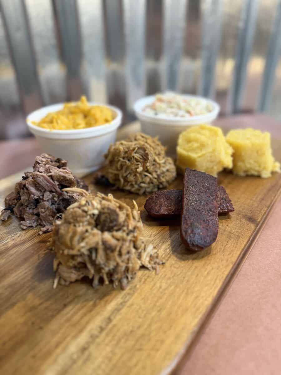 Smokehouse Sampler with sample portions of four smoked meats, two sides, and corn muffins on a wooden board