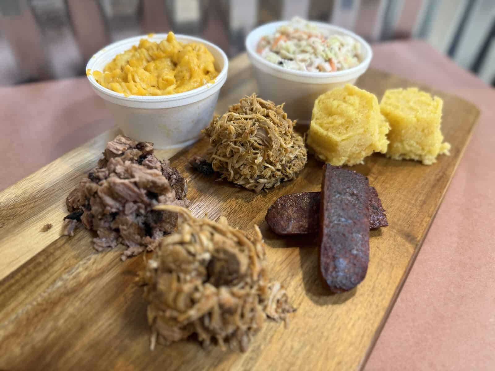 Honey's BBQ Smokehouse Sampler board with chopped brisket, pulled pork, pulled chicken, brisket sausage, corn muffins, mac and cheese, and coleslaw